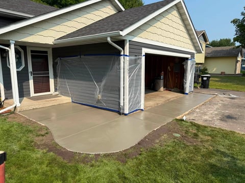 New concrete driveway and garage pad poured in front of residential home with gray siding