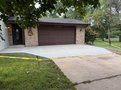New concrete driveway in front of brick house with garage and yellow caution tape