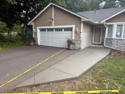Single-story house with white garage door, concrete driveway marked with yellow caution tape, and green lawn.
