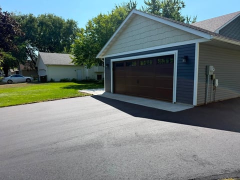 Modern two-car garage with dark brown door attached to residential home with driveway and green lawn