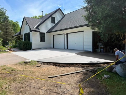 Two-story house with white siding and garage during driveway construction, with measurement tools visible