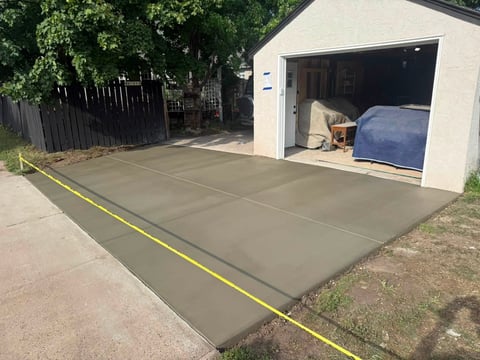 Newly poured concrete driveway in front of white garage with yellow tape marking the perimeter.