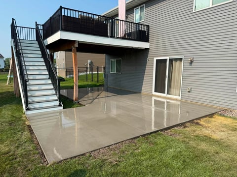 Modern two-story home with elevated deck, metal stairs, and polished concrete patio in grassy yard