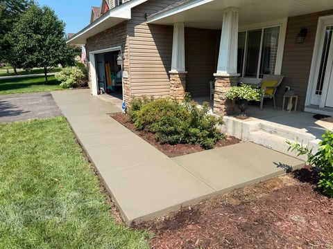 Front entry of brick home with large concrete patio, white columns, landscaping, and manicured lawn on sunny day
